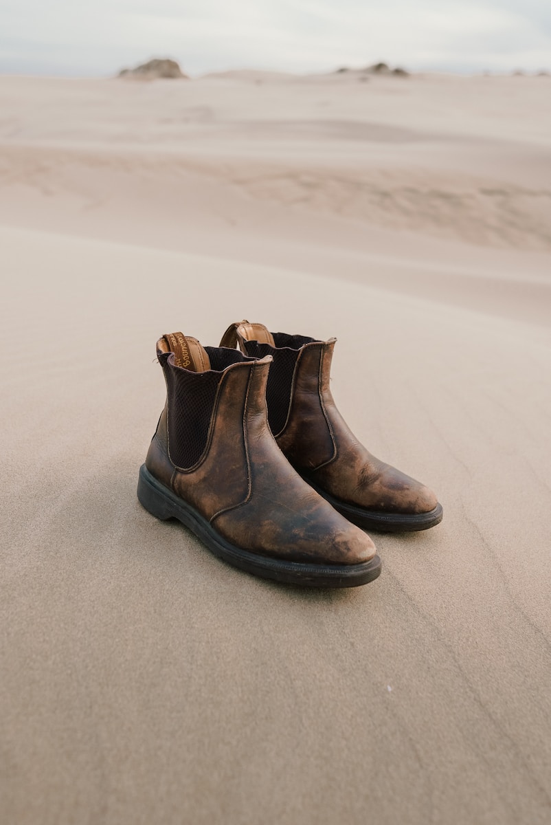 a pair of brown boots sitting on top of a sandy beach